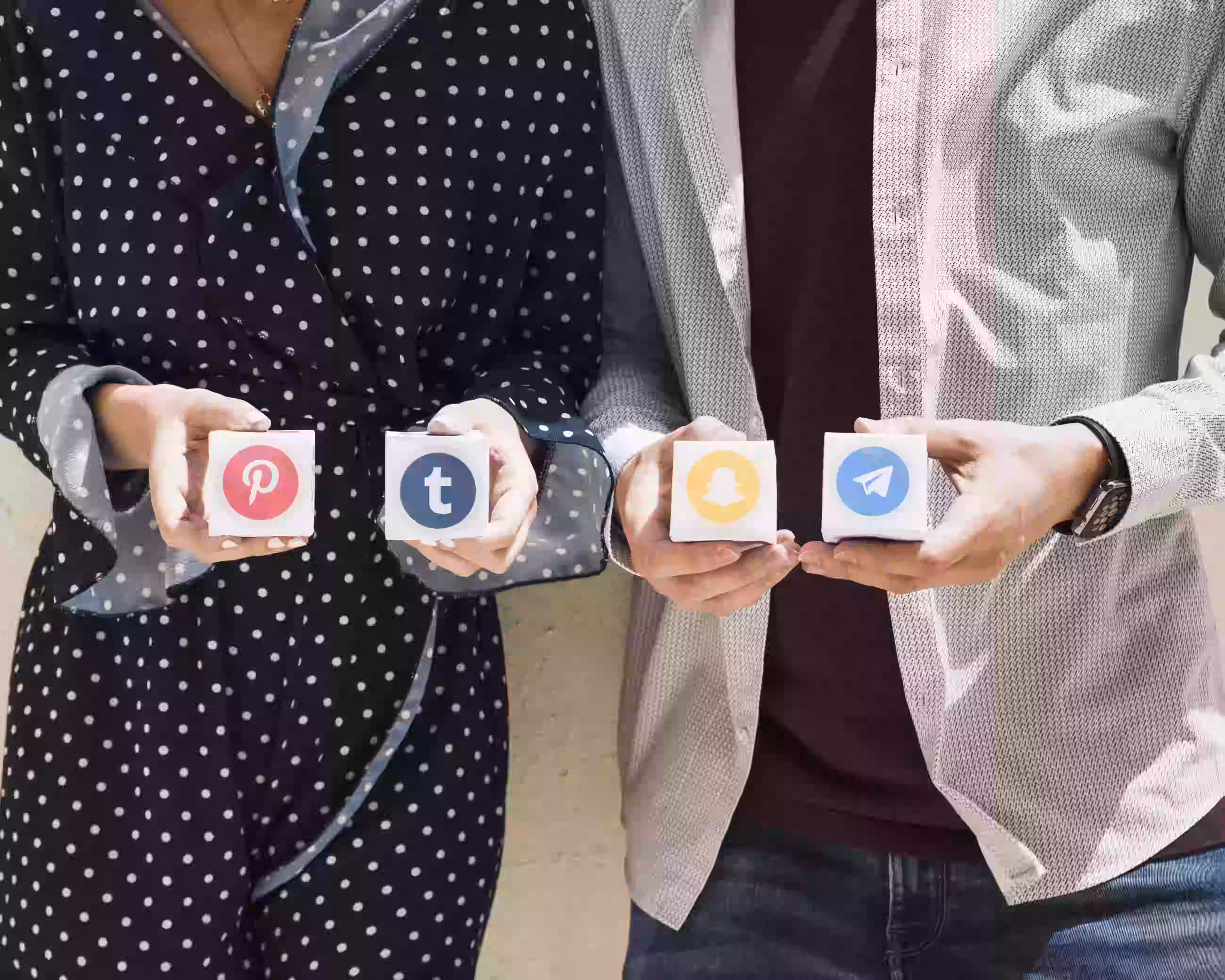 Dos personas sosteniendo iconos de plataformas sociales incluyendo Pinterest, Tumblr, Snapchat y Telegram
