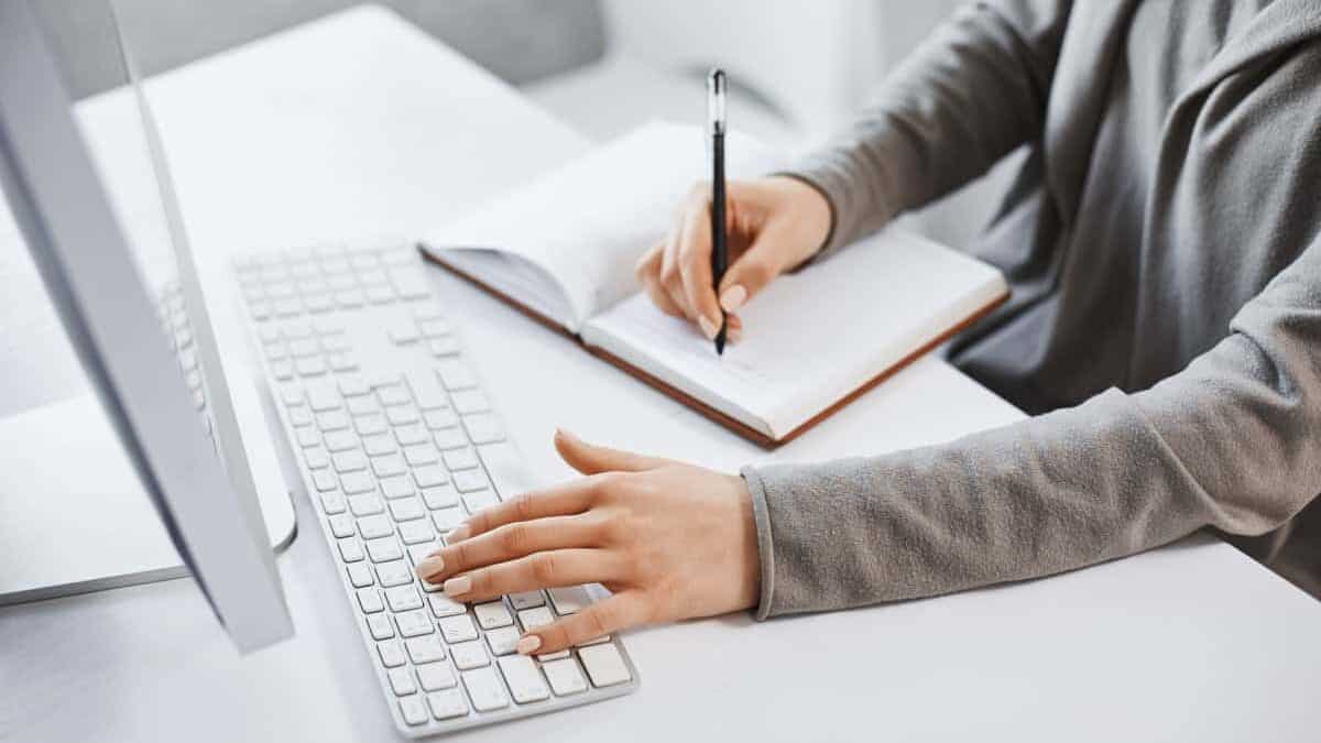 sieviete raksta uz datora un pieraksta piezīmes  